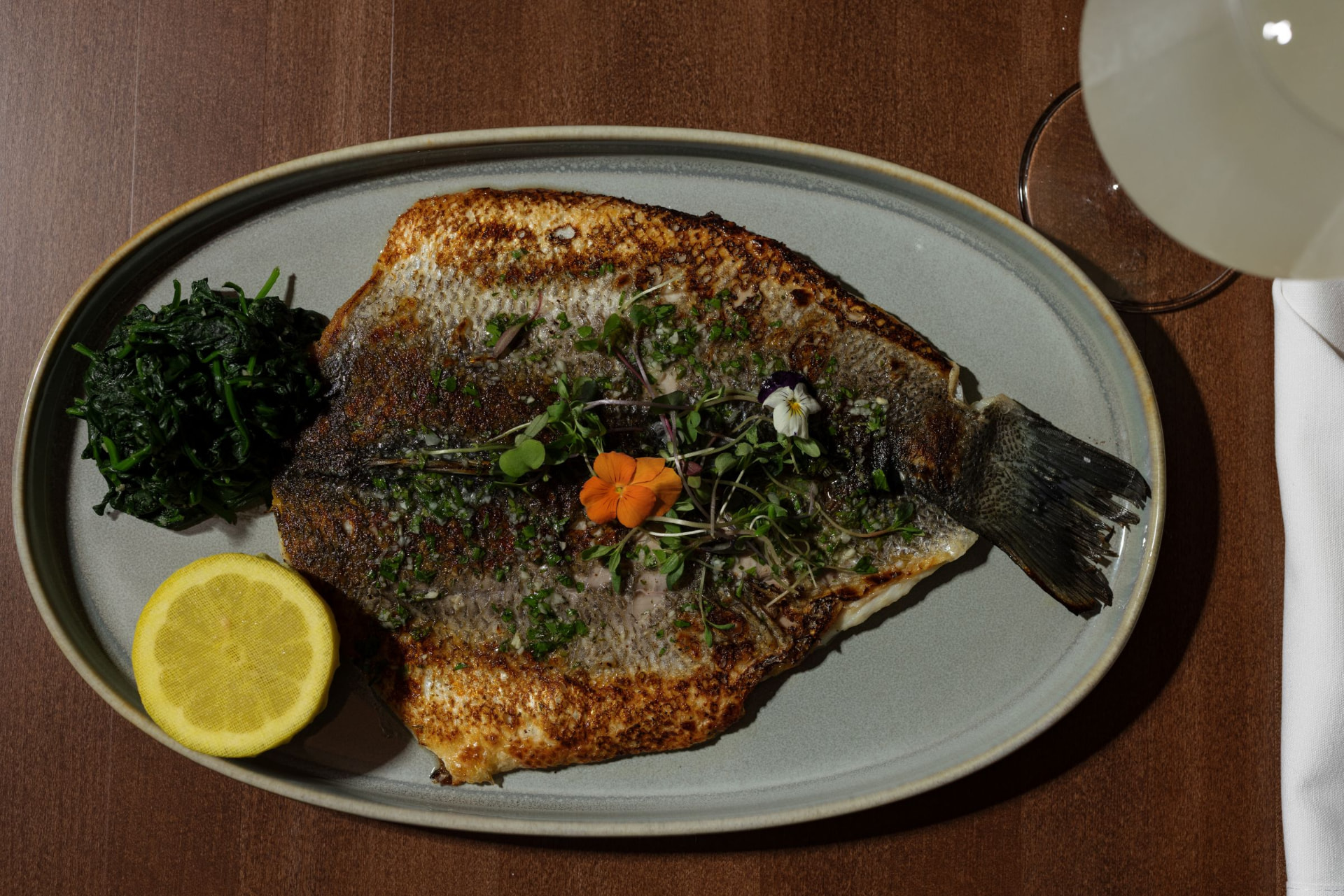 Whole Mediterranean branzino on an oval plate with blistered lemon and greens